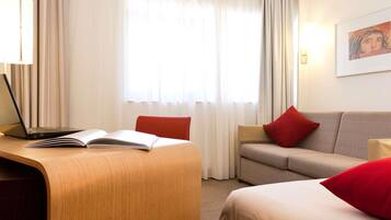 Habitación de hotel con escritorio, computadora portátil, libro abierto, dos sofás y una cama.