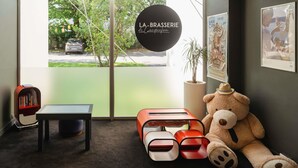 Un interior acogedor con un gran ventanal, un osito de peluche y un letrero que dice 'LA BRASSERIE'.