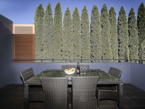 A dining area with a table and chairs, a decorative hedge, and a window with blinds.