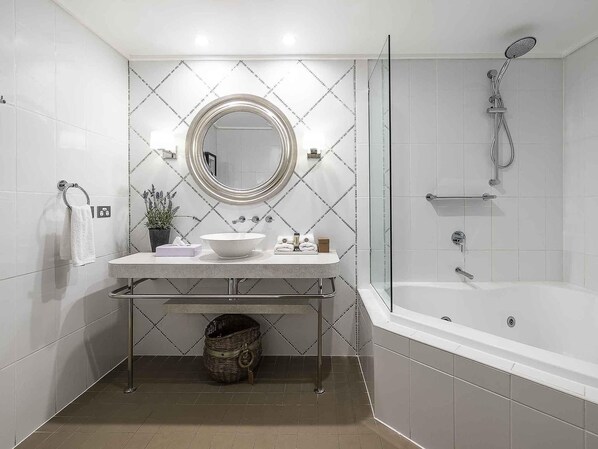 A modern bathroom with a freestanding bathtub, a round mirror, and a sink with a towel rack and a potted plant. - The Sebel Bowral Heritage Park (Bowral)