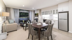 A modern kitchen with white cabinets, a stainless steel refrigerator, and a dining area with a wooden table and upholstered chairs. - The Sebel Bowral Heritage Park (Bowral)