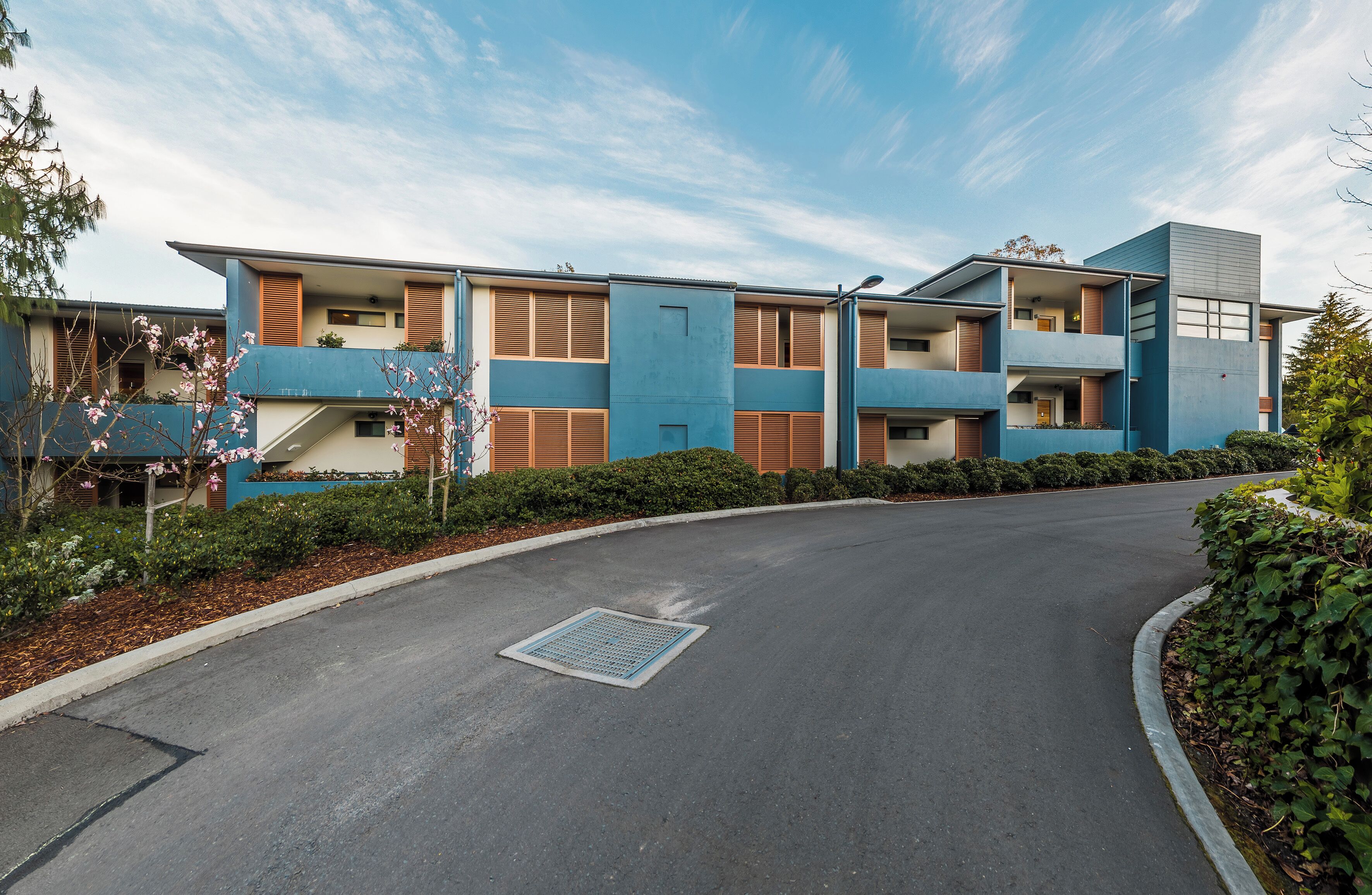 A modern multi-story building with a curved driveway leading to a gated entrance.