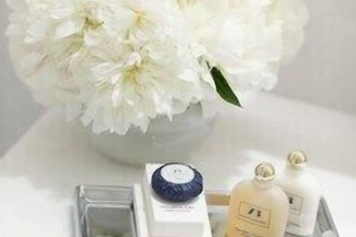 Une salle de bain avec un bouquet de fleurs blanches, un plateau contenant des articles de toilette et un miroir.