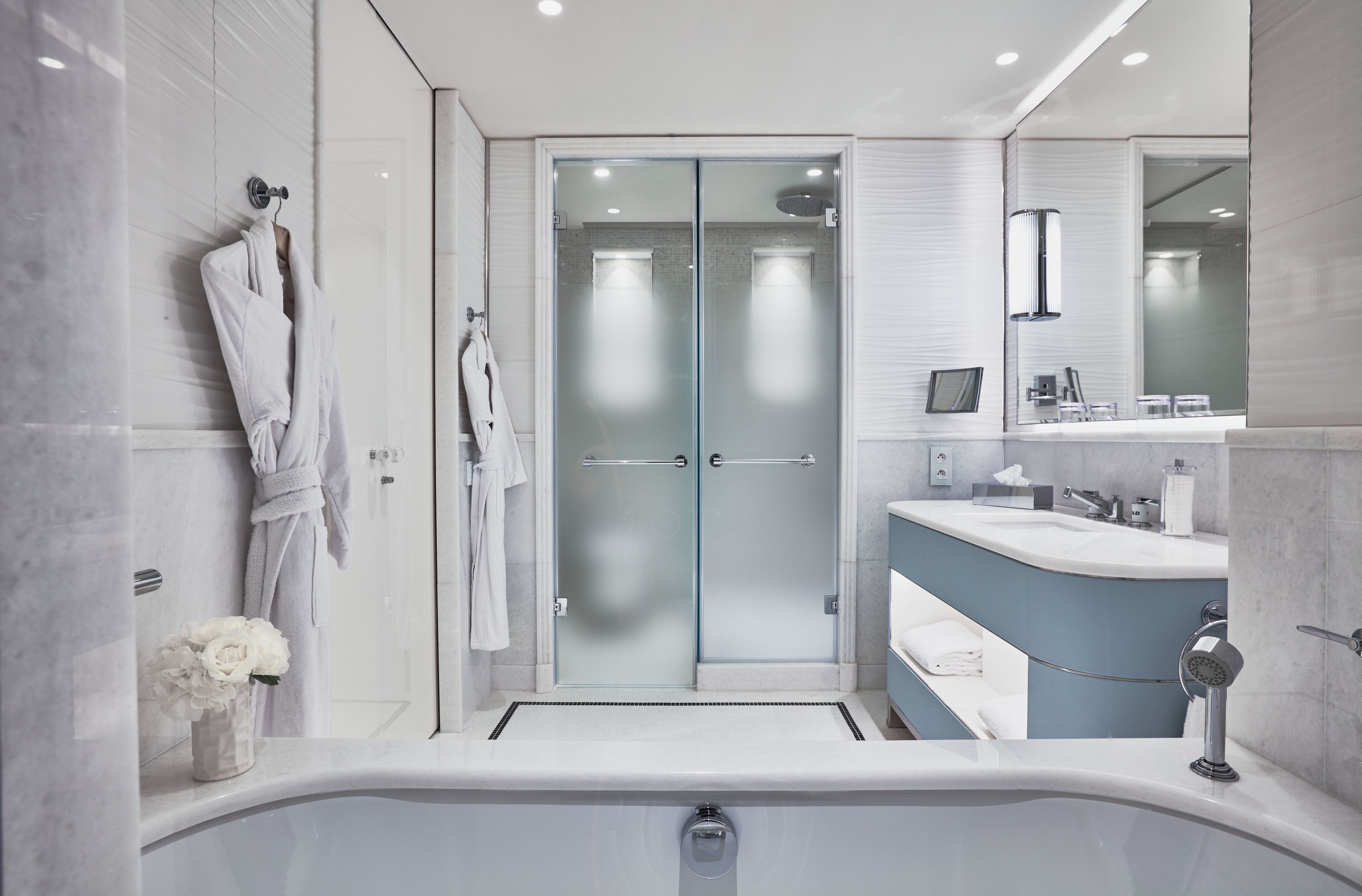 A modern bathroom with a glass-enclosed shower, a white bathtub, and a vanity with a blue countertop.