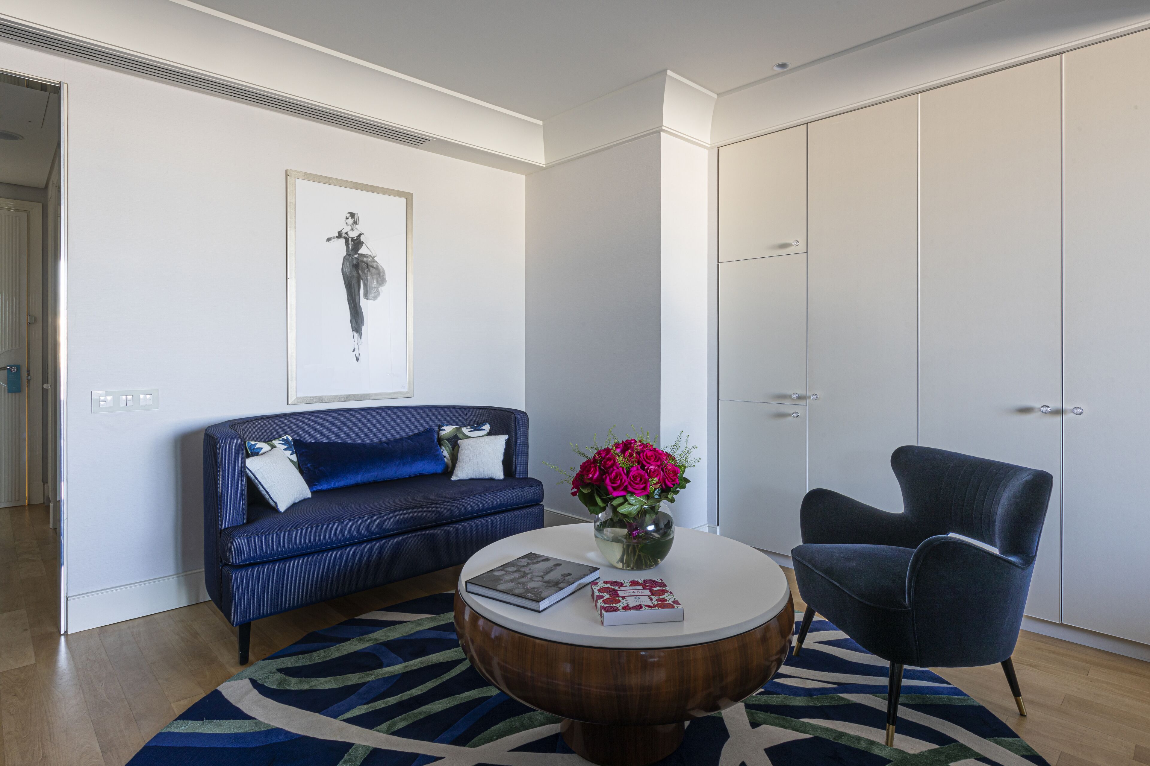 A modern living room with a blue sofa, a round wooden coffee table, and a blue armchair.