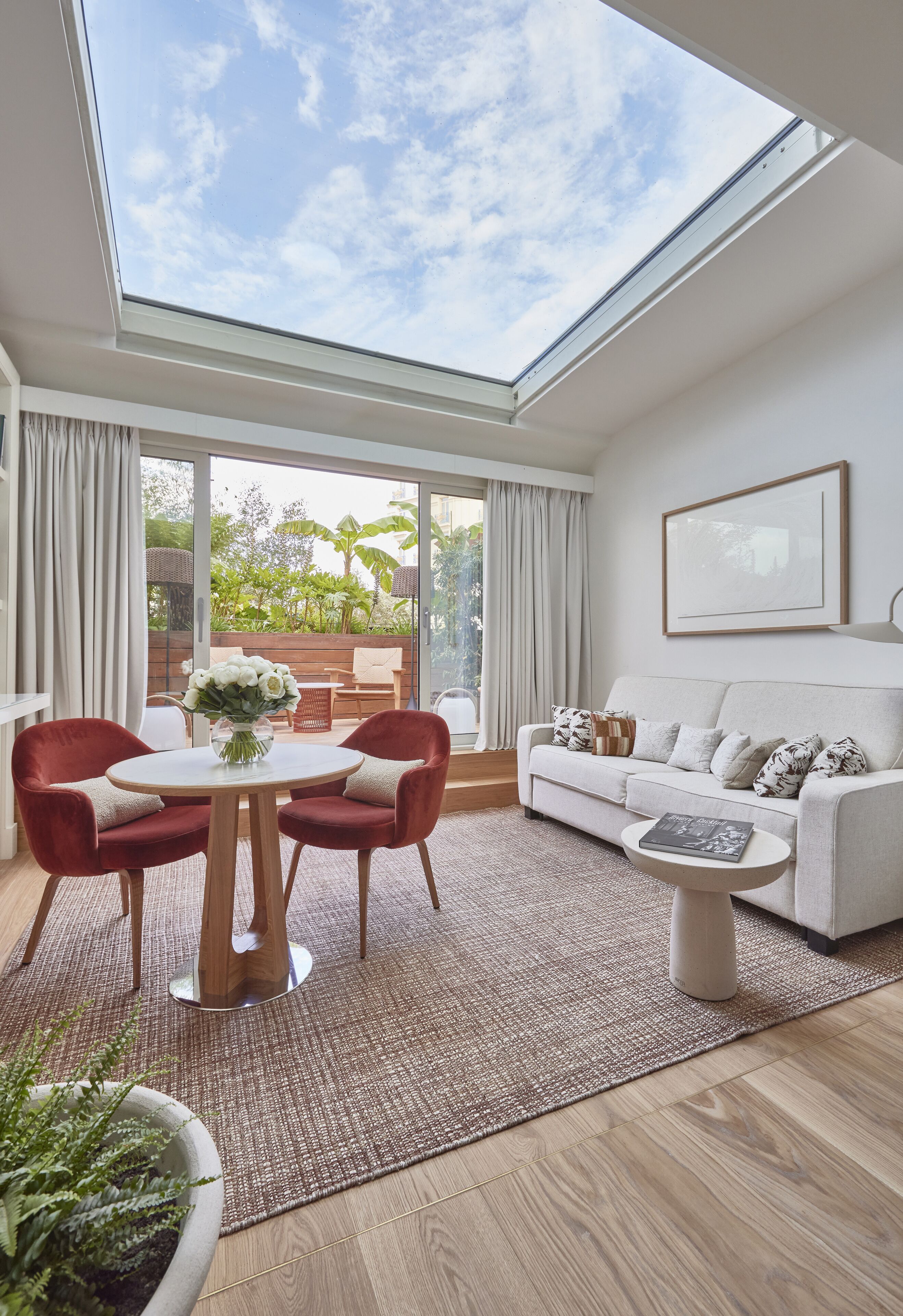 A modern living room with a skylight, a dining area with red chairs, a white sofa, and a coffee table.