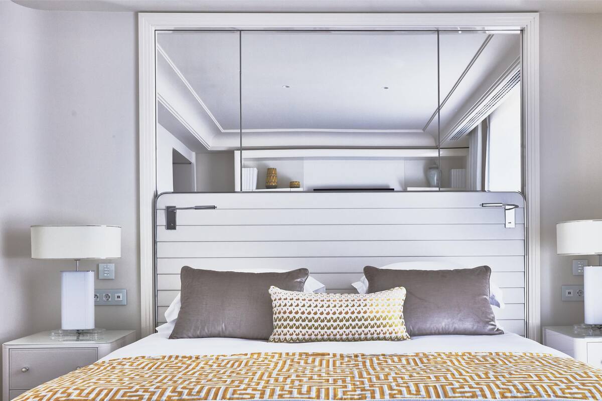 Une chambre d’hôtel moderne dotée d’un grand lit, de deux tables de chevet, d’une commode, d’un miroir et d’une armoire intégrée.