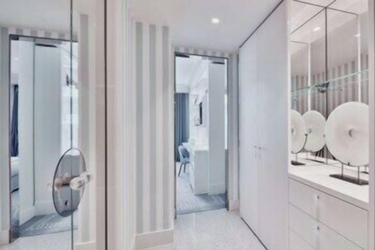 Un couloir d’hôtel moderne avec une porte en verre, un espace salon et un objet circulaire fixé au mur.