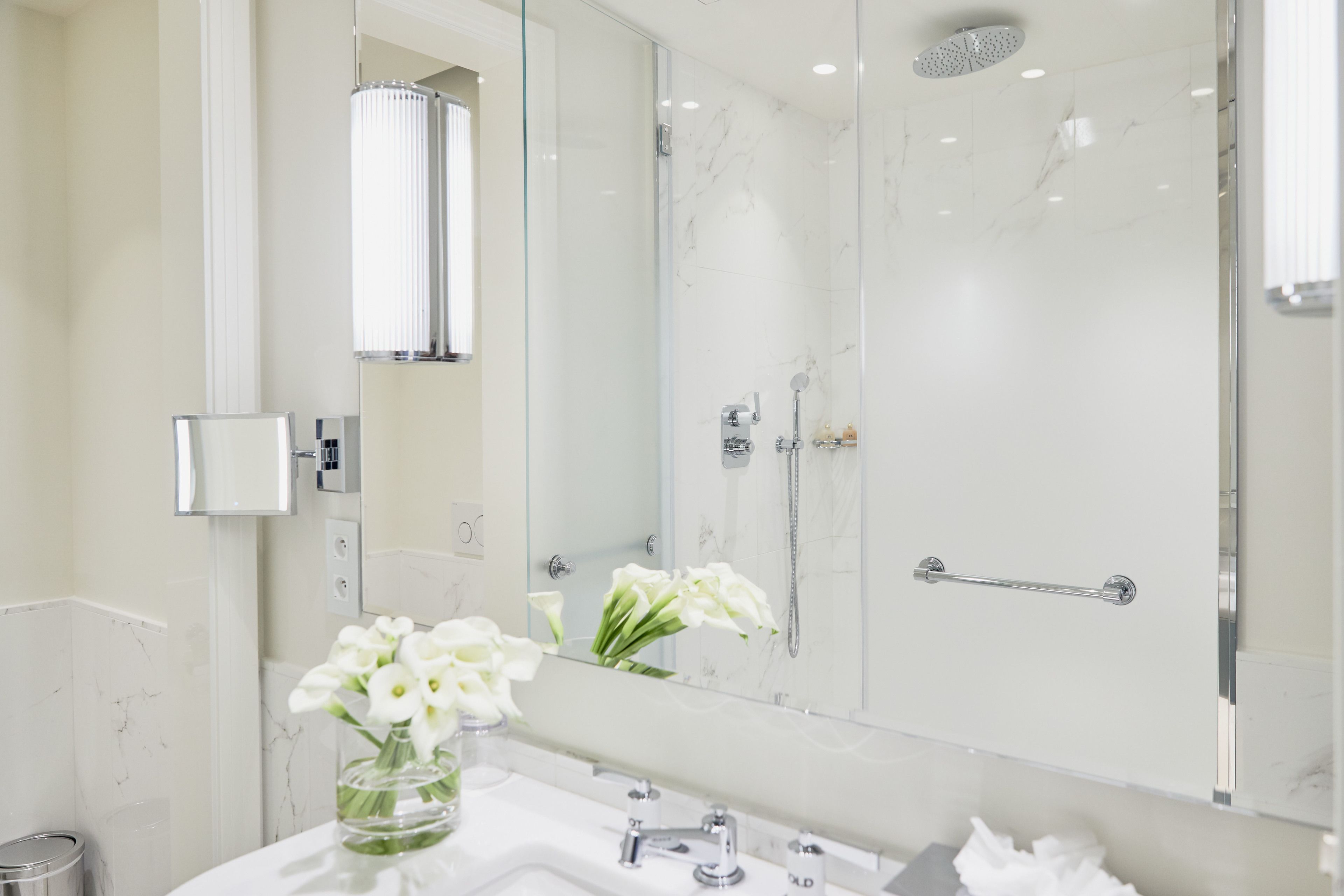 A modern bathroom with a glass shower enclosure, a white marble sink, and a mirror reflecting the shower.