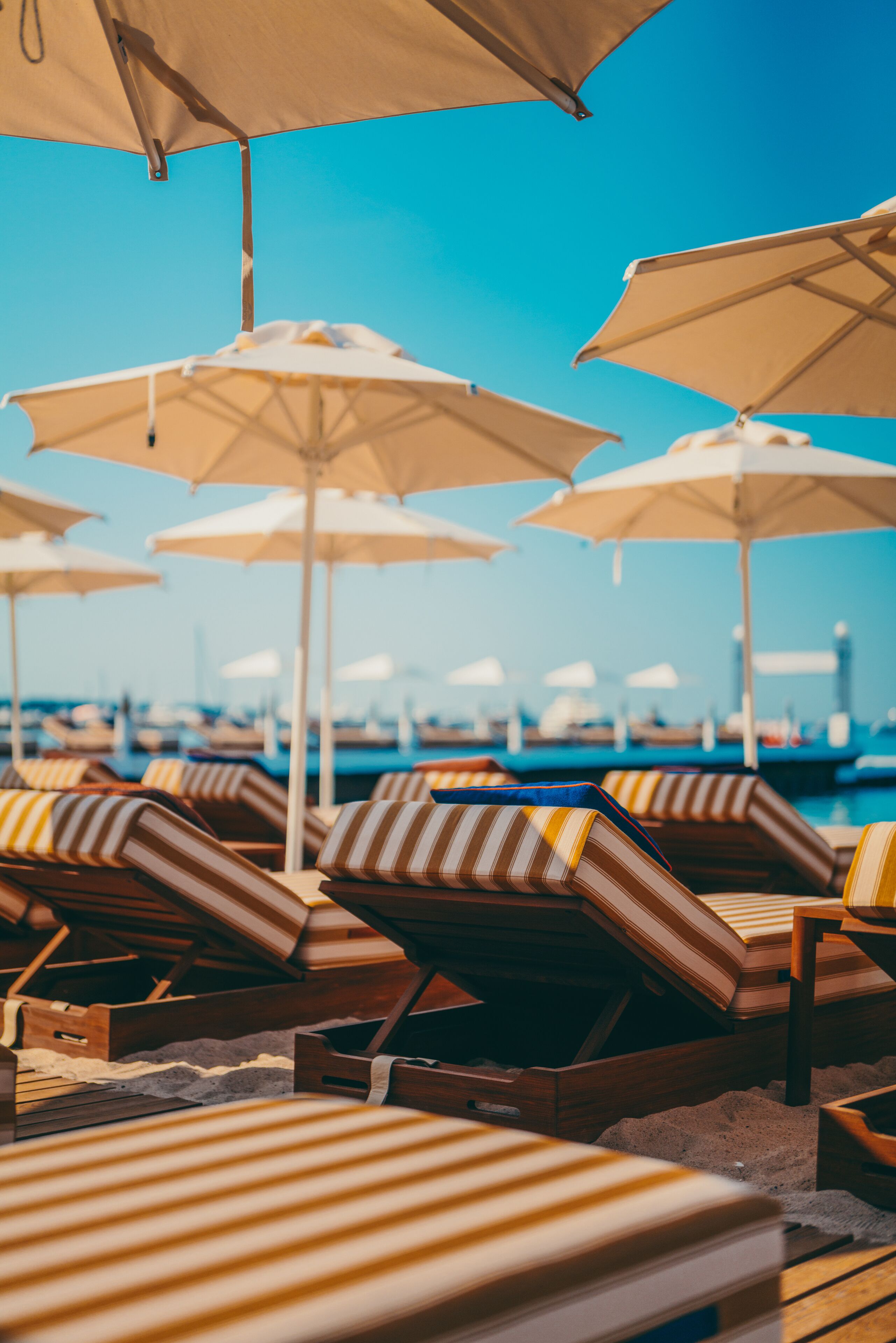 Un espace de détente aménagé sur la plage, avec des chaises longues à rayures et des parasols de couleur beige.