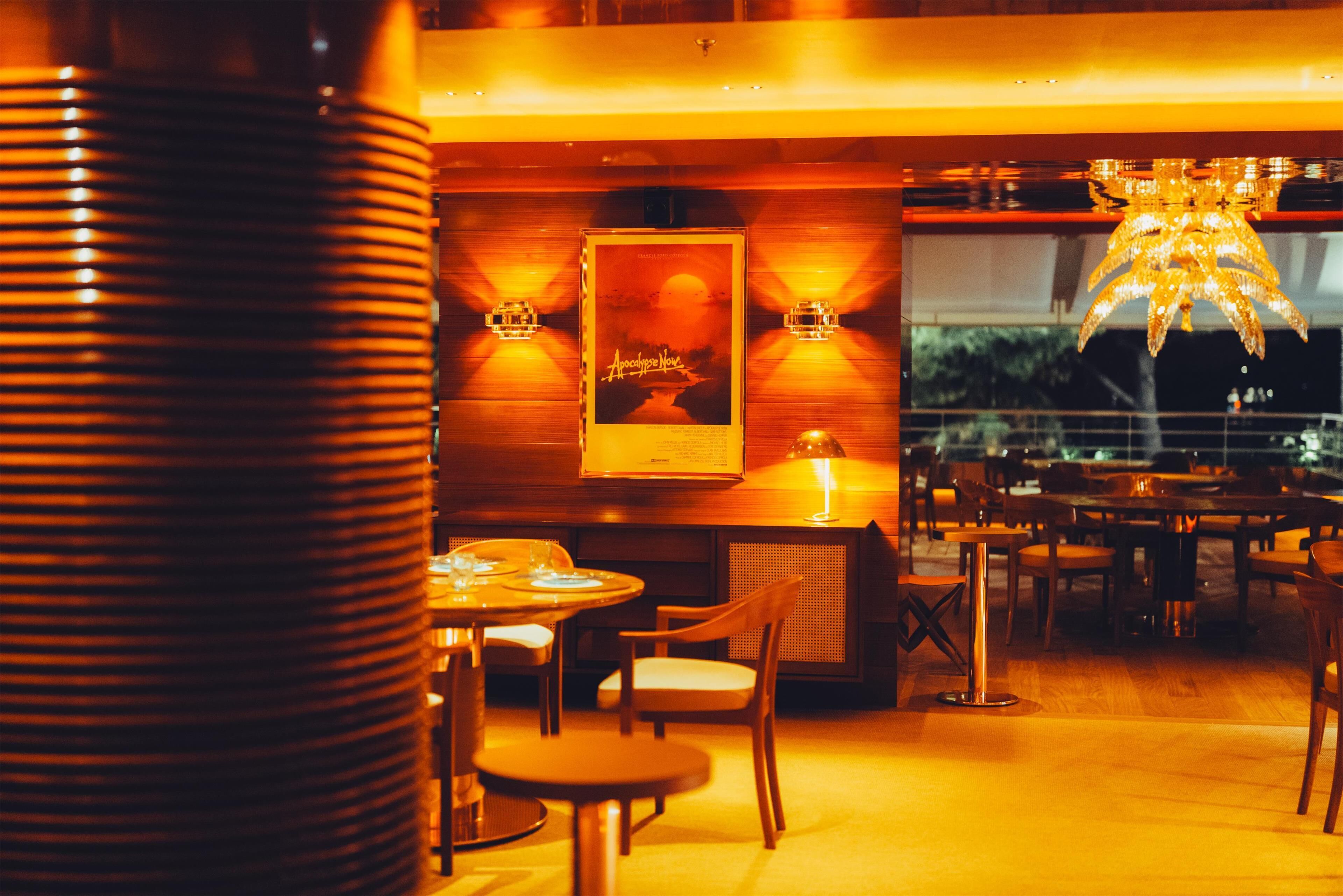 A restaurant with wooden tables and chairs, a poster on the wall, and a chandelier.