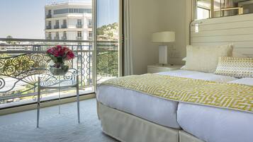 Une chambre d’hôtel avec un grand lit, une table de chevet, une lampe, une fenêtre donnant sur des immeubles et une chaise agrémentée d’un vase de fleurs.