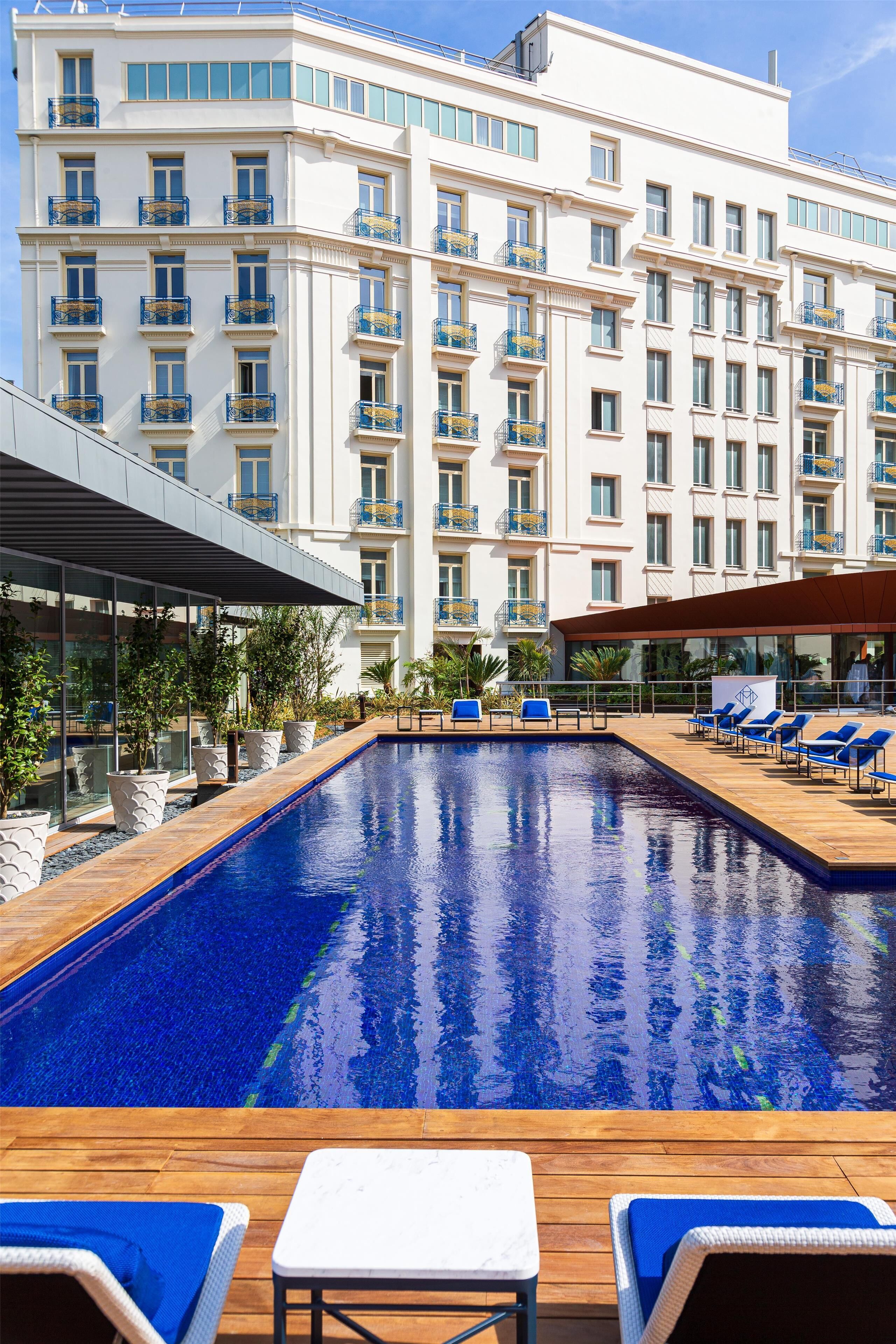 Een hotel met een zwembad, ligbedden en een overdekt terras.