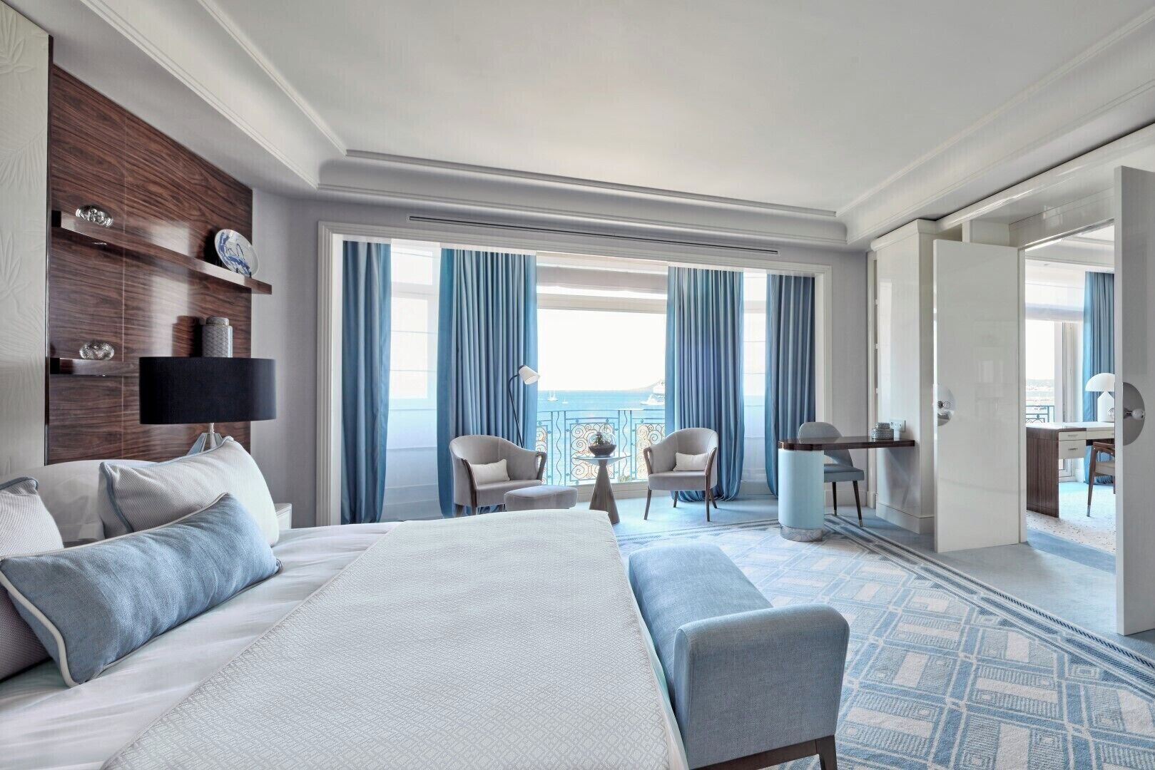 A hotel room with a large bed, two armchairs, a desk, and a view of the sea.