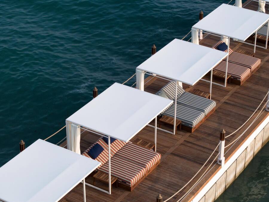 A deck with multiple white canopied seating areas, each with striped cushions and wooden flooring.