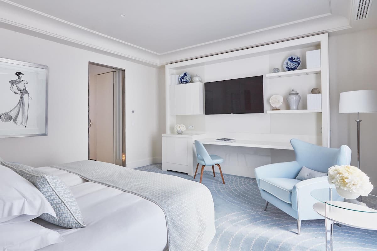 Une chambre d’hôtel moderne équipée d’un lit, d’un bureau, d’une chaise, d’une télévision et d’une petite table sur laquelle est posé un vase.