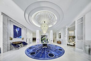 A spacious lobby with a central chandelier, a circular blue carpet, and a modern fireplace.