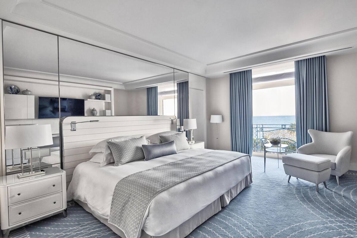 Une chambre d’hôtel moderne dotée d’un grand lit, d’un bureau, d’une chaise, d’un balcon avec vue et d’un grand miroir.