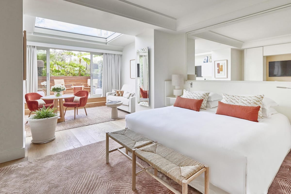 Une chambre d’hôtel moderne dotée d’un grand lit, d’une banquette, d’un coin repas avec une table et des chaises, et offrant une vue sur l’extérieur.