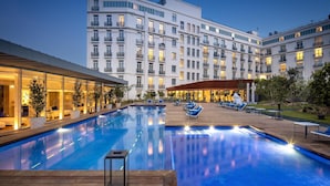 A hotel with a swimming pool, outdoor seating, and a large building with balconies.