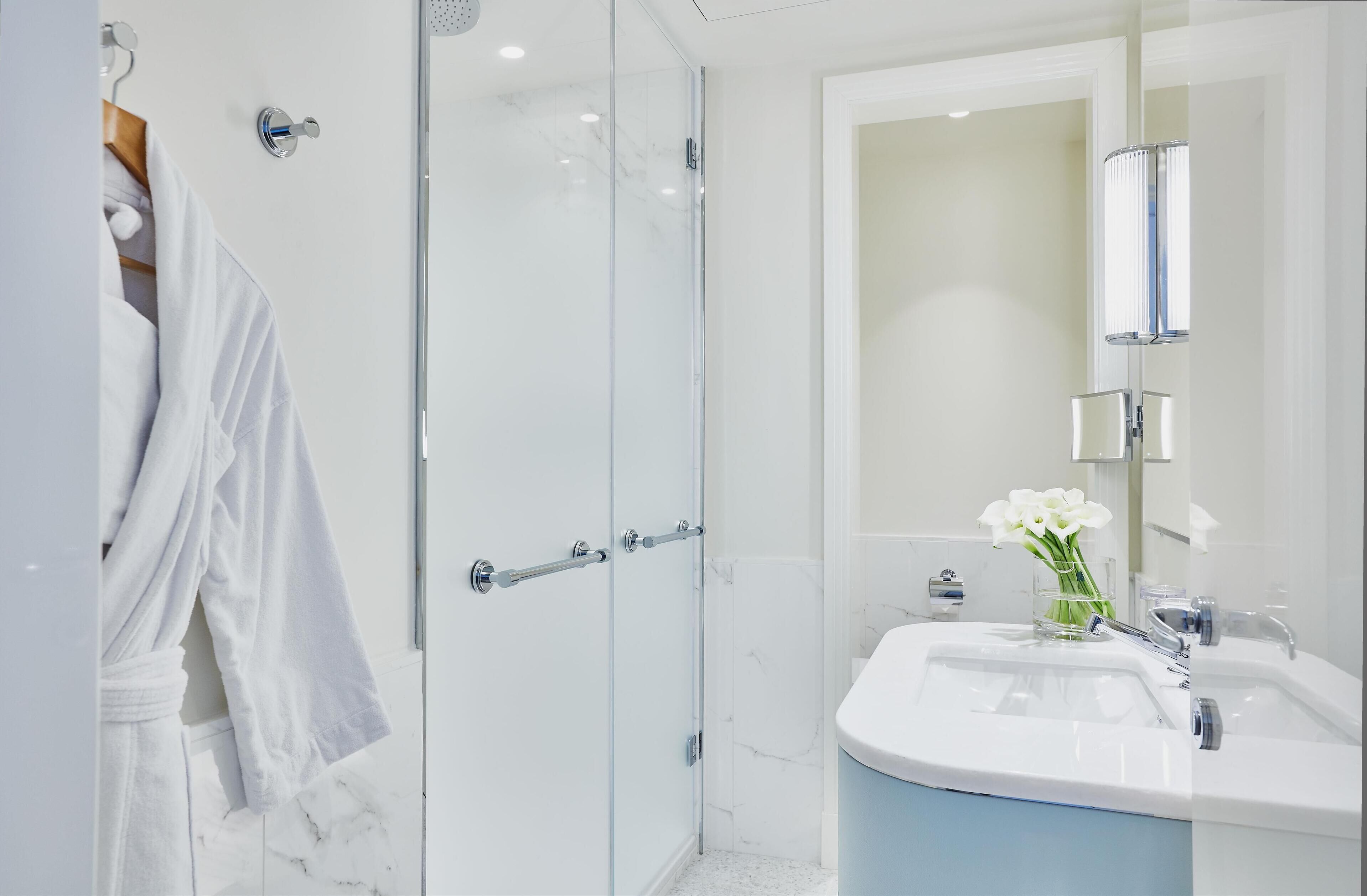 Un baño moderno con cabina de ducha de vidrio, un lavabo blanco con encimera azul y un espejo con luz integrada.