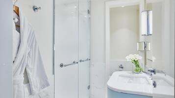 Un baño moderno con cabina de ducha de vidrio, un lavabo blanco con encimera azul y un espejo con luz integrada.