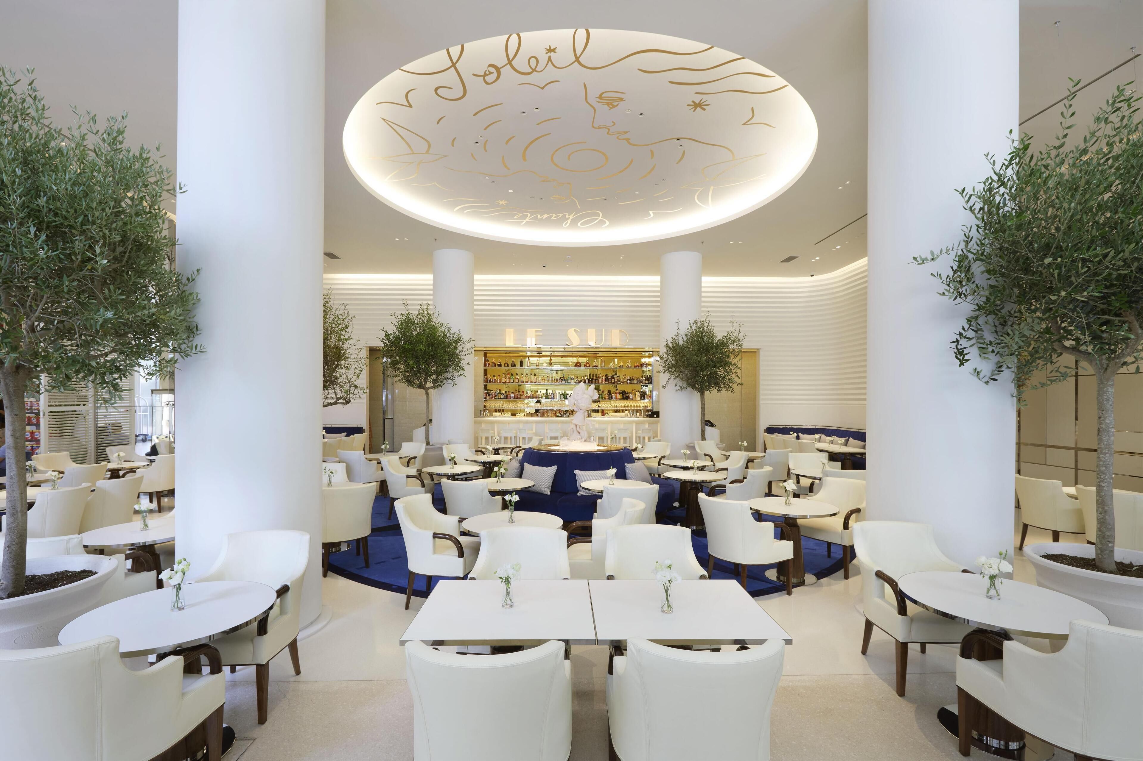 A spacious indoor dining area with white tables and chairs, a central bar area, and decorative ceiling with gold script.