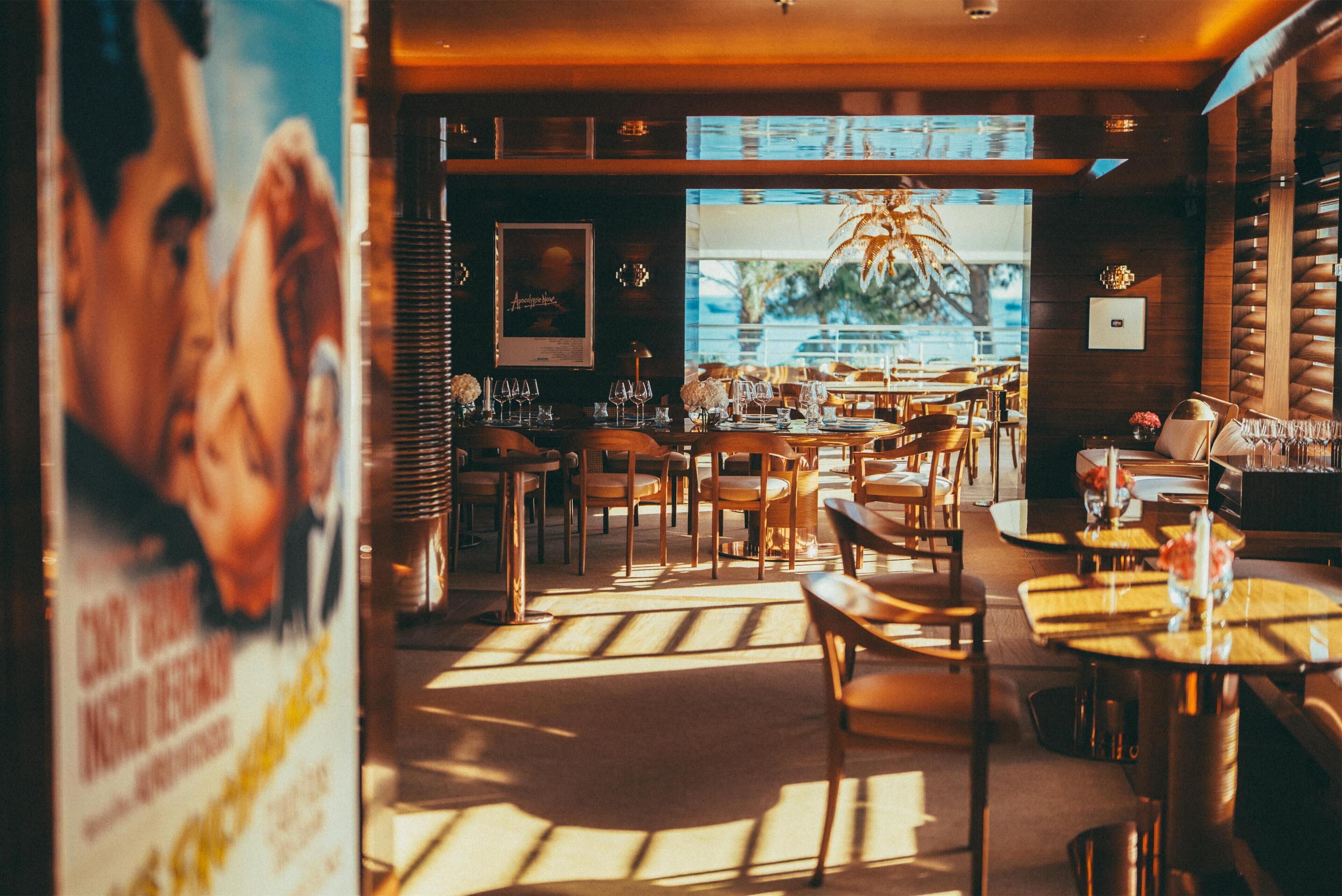 A restaurant interior with wooden tables and chairs, a large window with a view, and a poster on the wall.