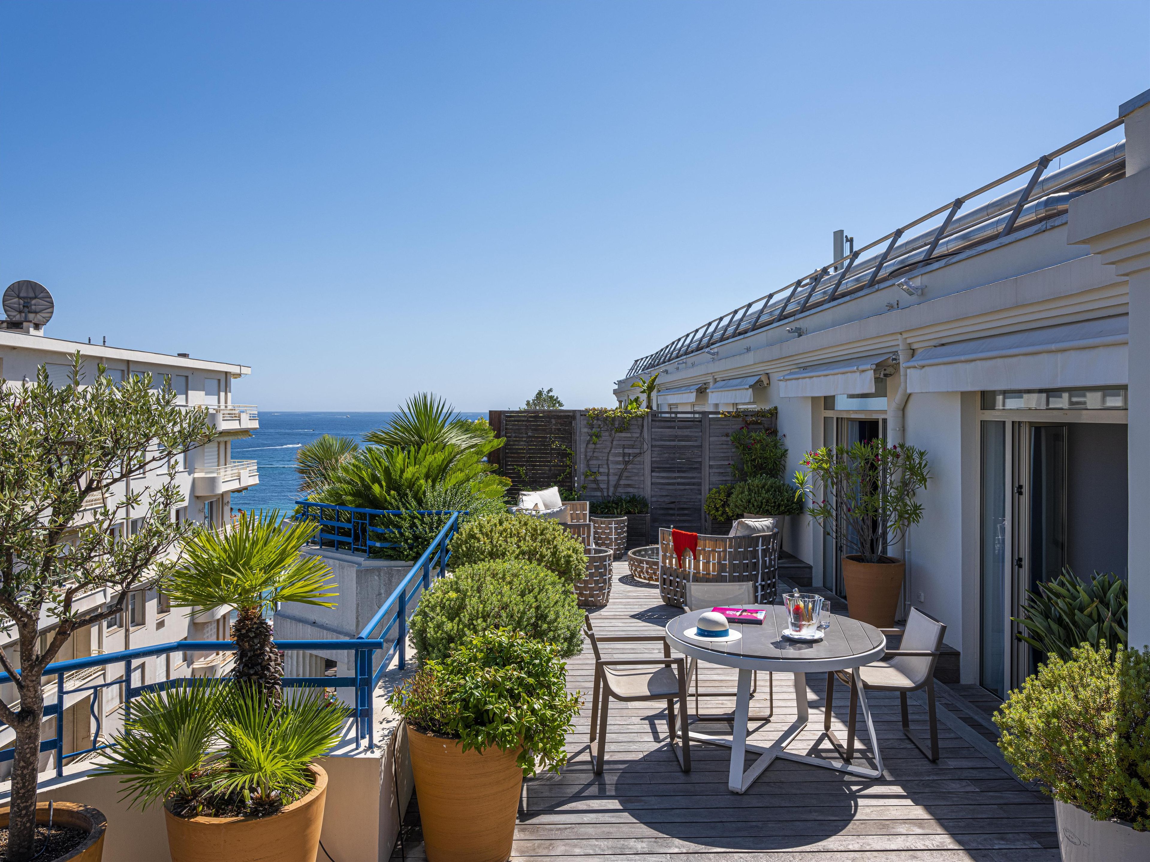 Une terrasse avec une table et des chaises, entourée de plantes en pot et offrant une vue sur la mer.