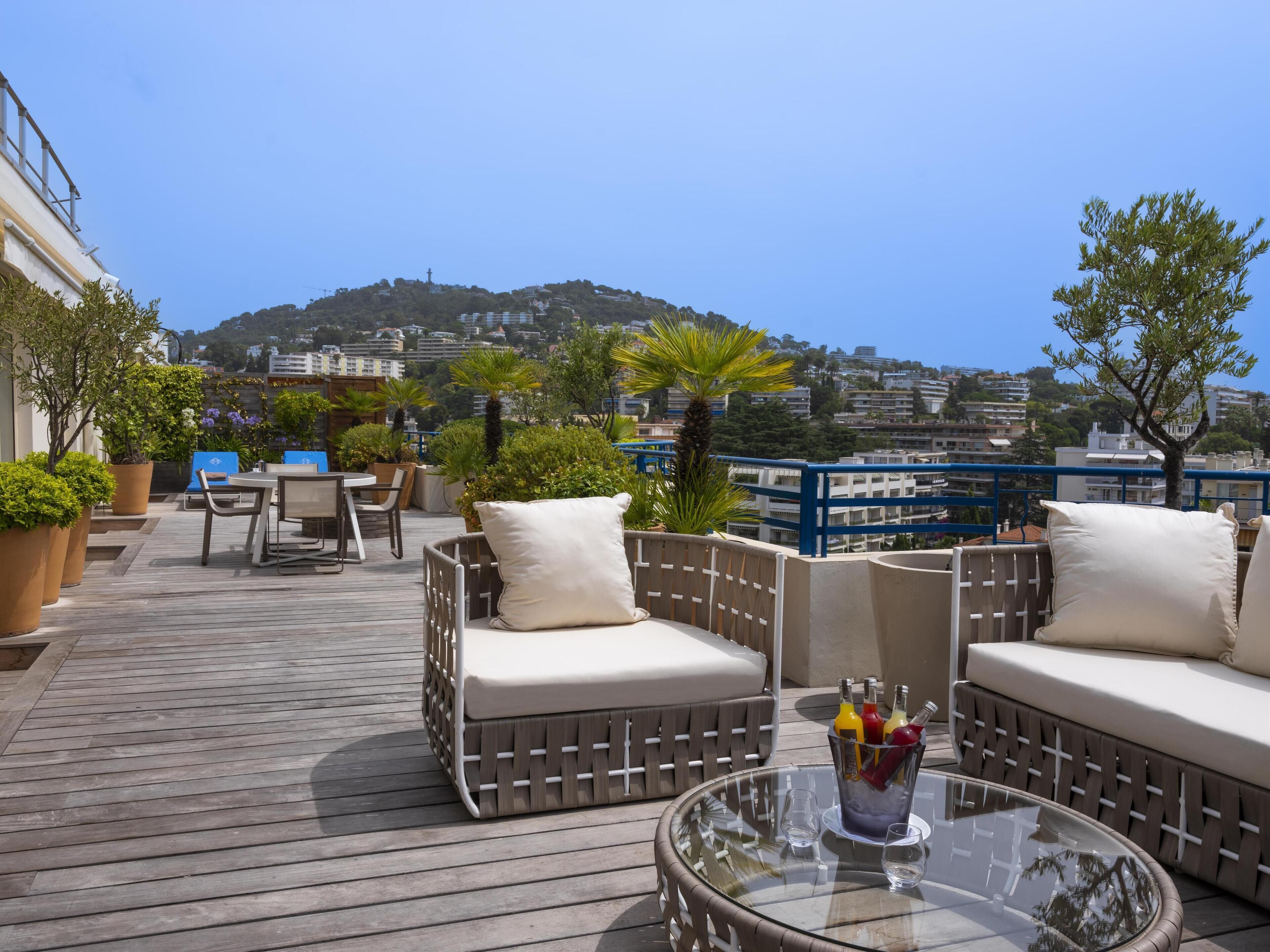 Terraza en la azotea con mobiliario de mimbre, una mesa de vidrio y vistas a un paisaje urbano.