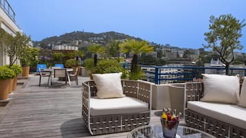 Terraza en la azotea con mobiliario de mimbre, una mesa de vidrio y vistas a un paisaje urbano.