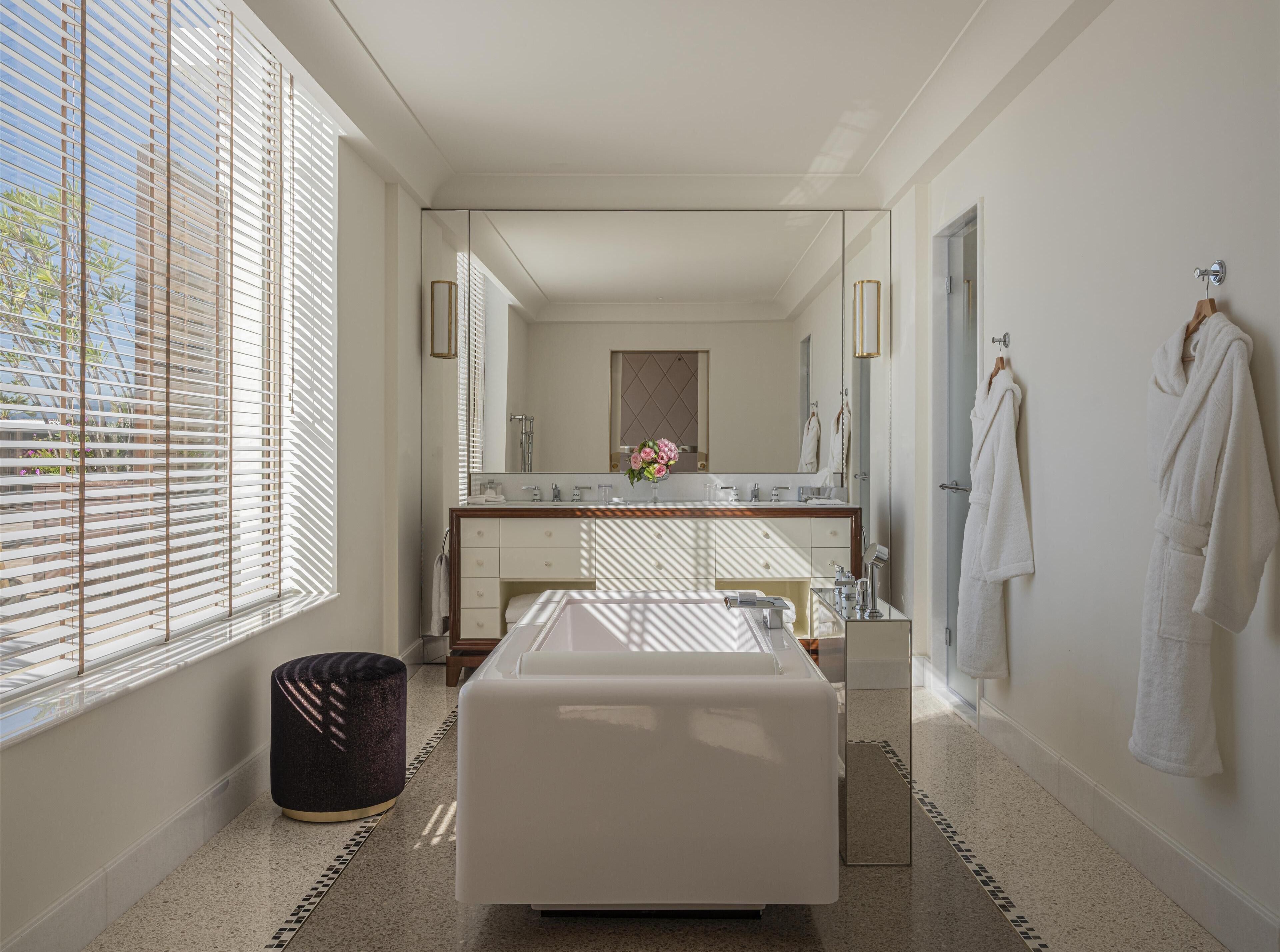 A modern bathroom with a large mirror, a bathtub, and a vanity.