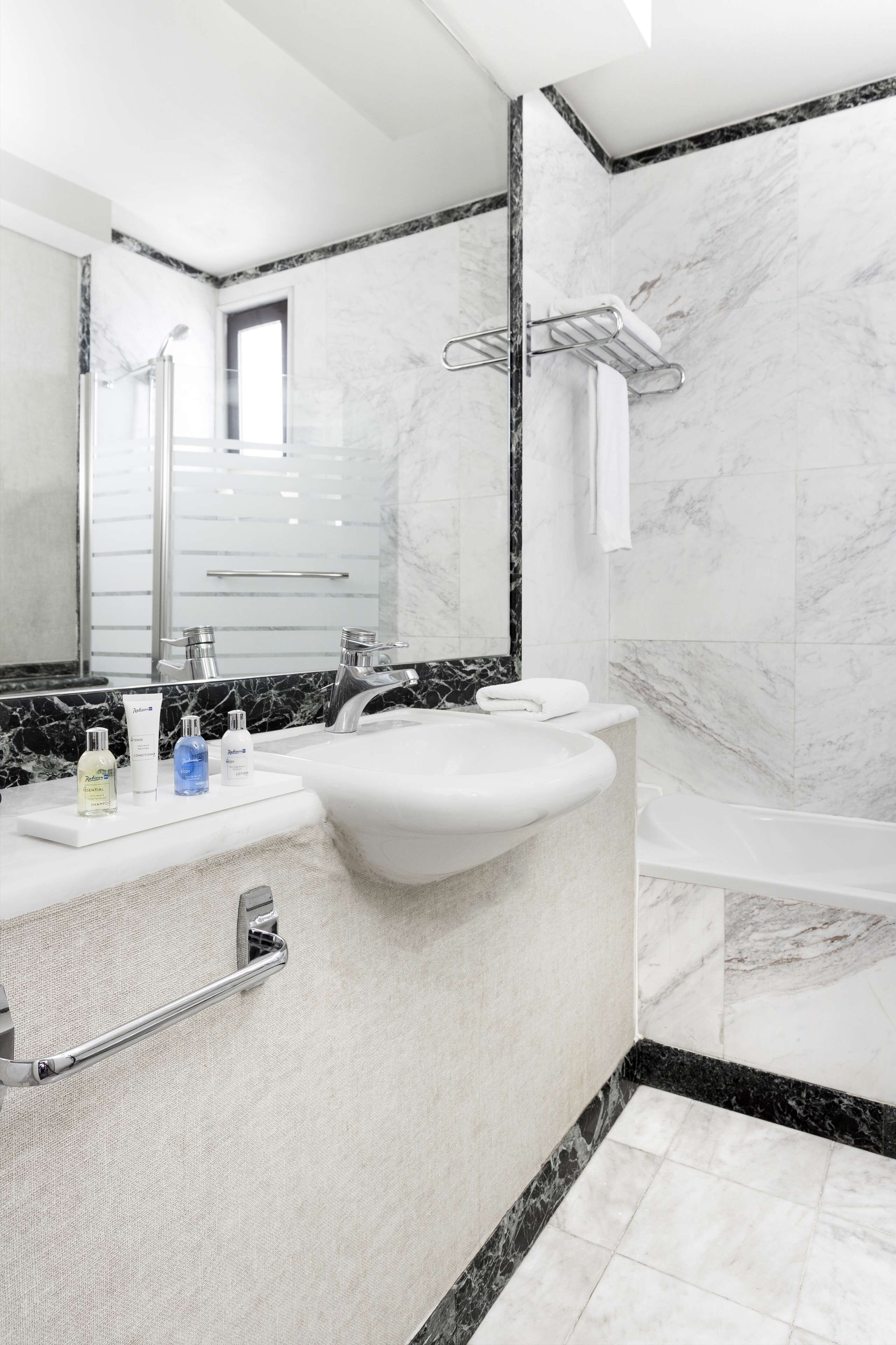 Une salle de bain moderne avec un grand lavabo, deux miroirs, une baignoire et des murs en marbre.
