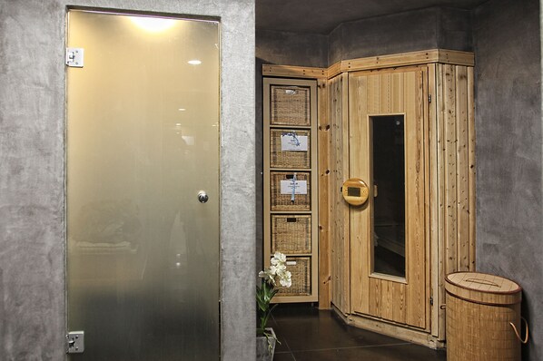A sauna room with a wooden cabinet, a glass door, and a small trash bin.