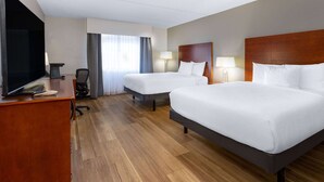 Una habitación de hotel con dos camas, un escritorio con televisor y una silla.