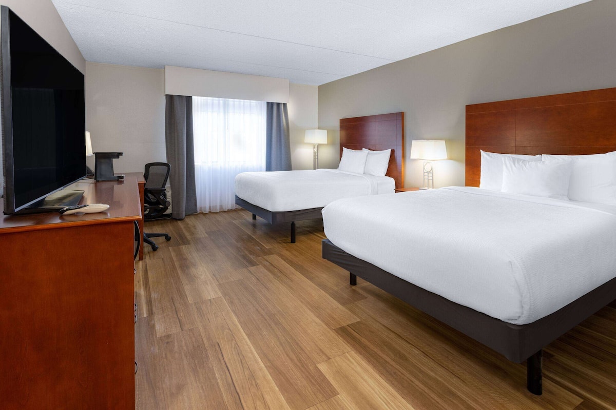 A hotel room with two beds, a desk with a television, and a chair.