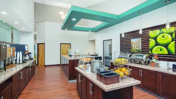 A modern hotel kitchen with a breakfast bar, coffee machines, and a large poster advertising 'La Quinta'.