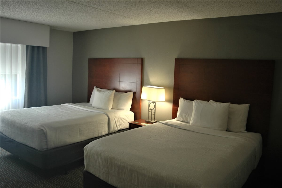 A hotel room with two beds, a nightstand with a lamp, and a window with curtains.