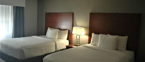 A hotel room with two beds, a nightstand with a lamp, and a window with curtains.