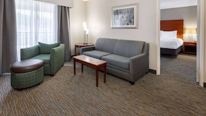 Una habitación de hotel con sofá, sillón, mesita y cama con cabecera.