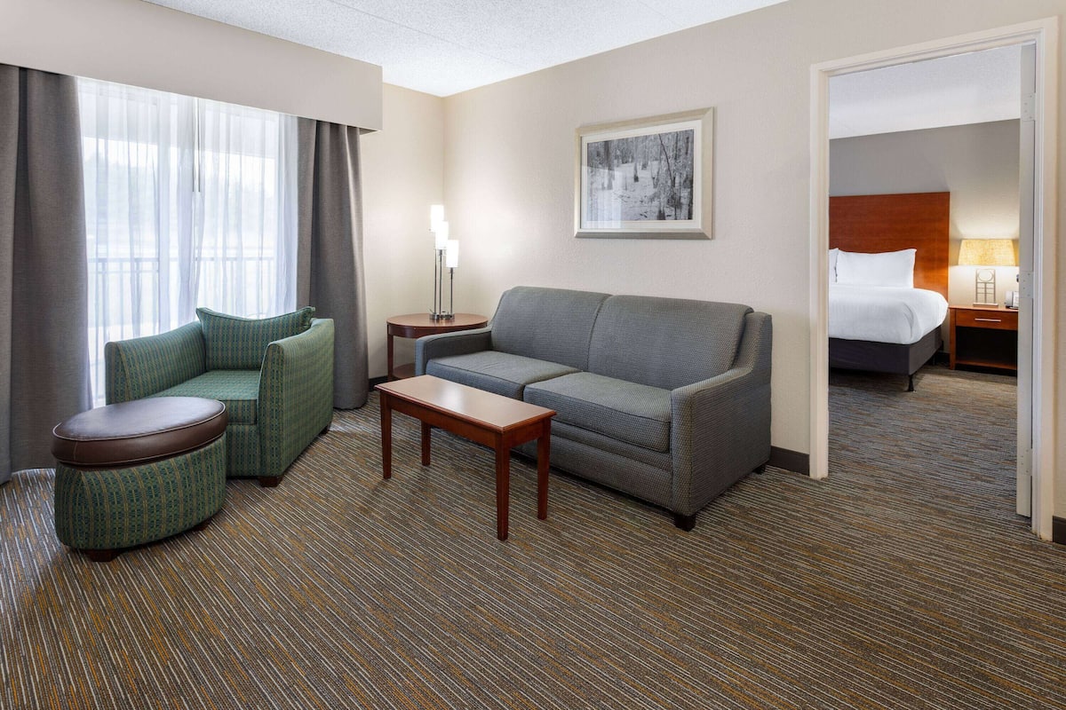 A hotel room with a sofa, armchair, small table, and a bed with a headboard.