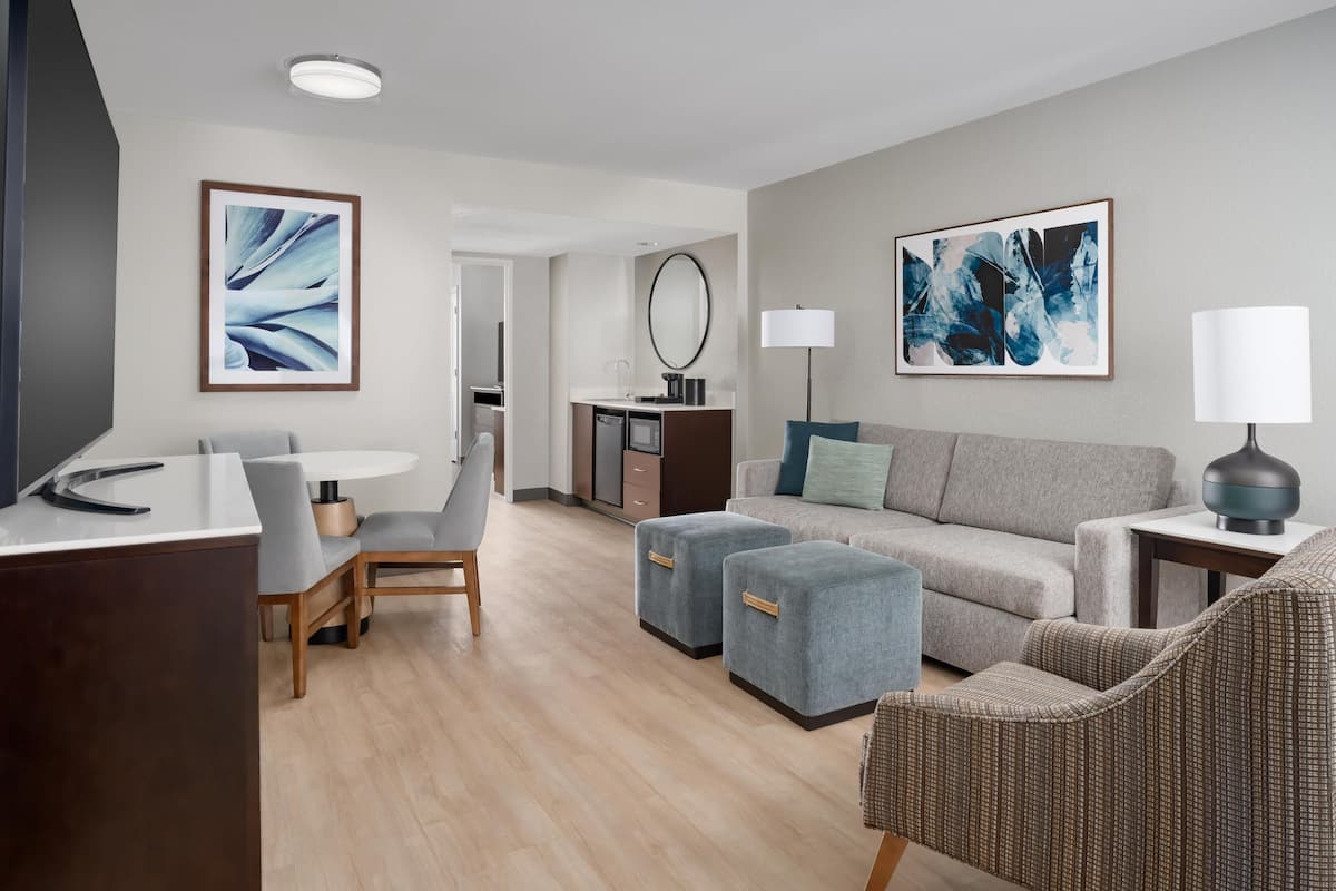 Una habitación de hotel moderna con comedor, un conjunto de sofás y obras de arte en las paredes.