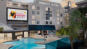 A hotel with a swimming pool, outdoor seating, and a sign for the Walt Disney World Good Neighbor Hotel.