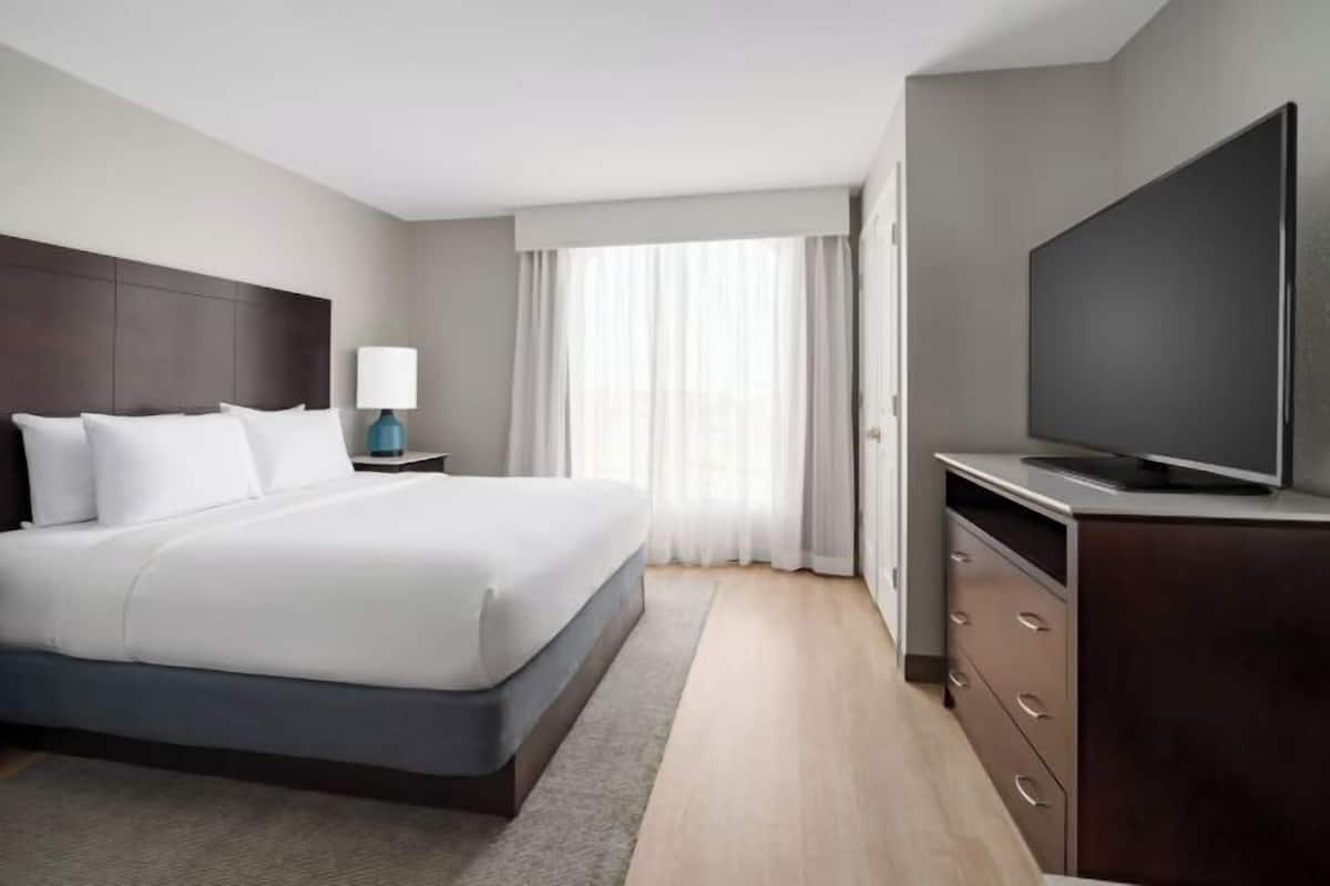 Una habitación de hotel con una cama, televisor, mesita de noche y cómoda.
