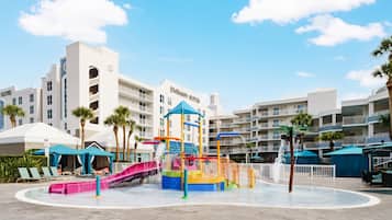 A water park with slides and a play structure, surrounded by hotel buildings with balconies.