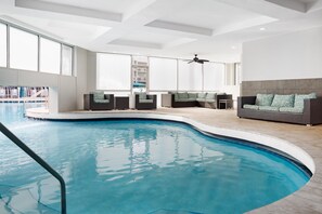 Un espace piscine intérieur moderne, doté d’une piscine aux lignes courbes, de coins salon et d’un ventilateur de plafond.