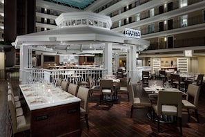 A modern hotel lobby with a central bar area, multiple dining tables, and a multi-level balcony. - Embassy Suites by Hilton Orlando Lake Buena Vista Resort (Orlando)