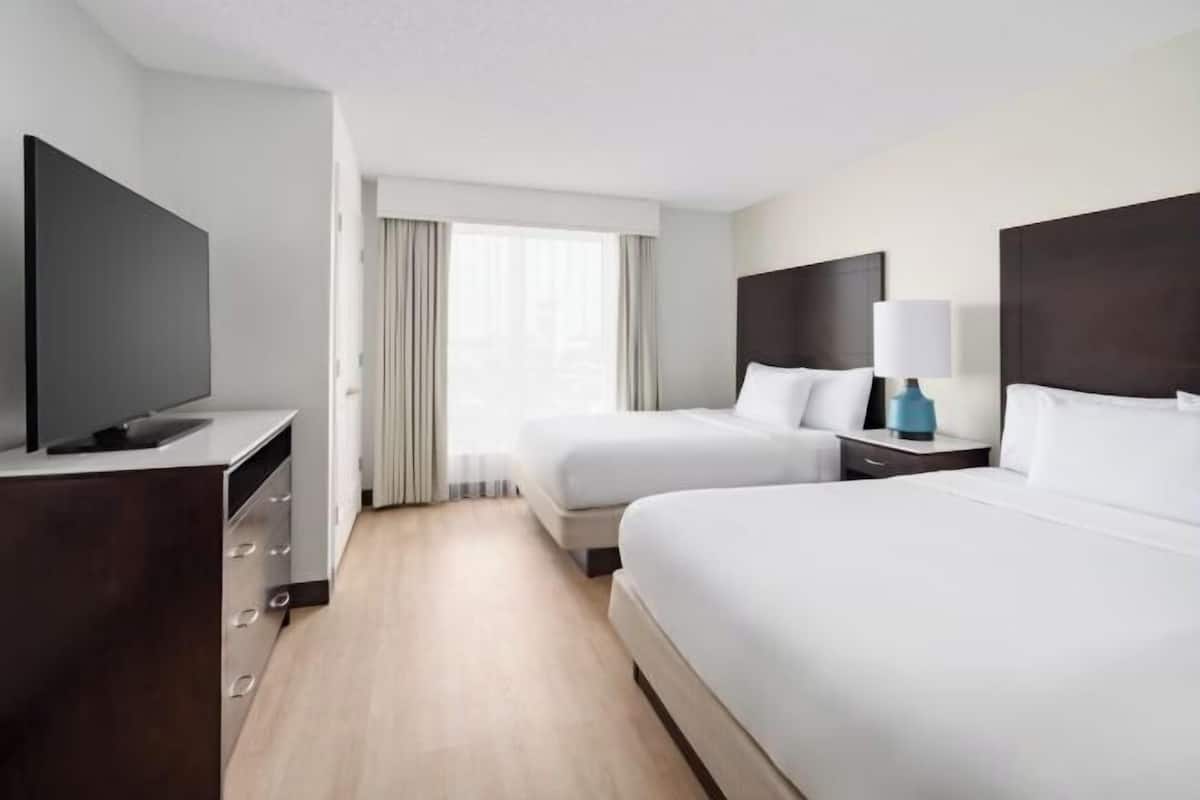 Habitación de hotel con televisión, dos camas, escritorio y ventana con cortinas.