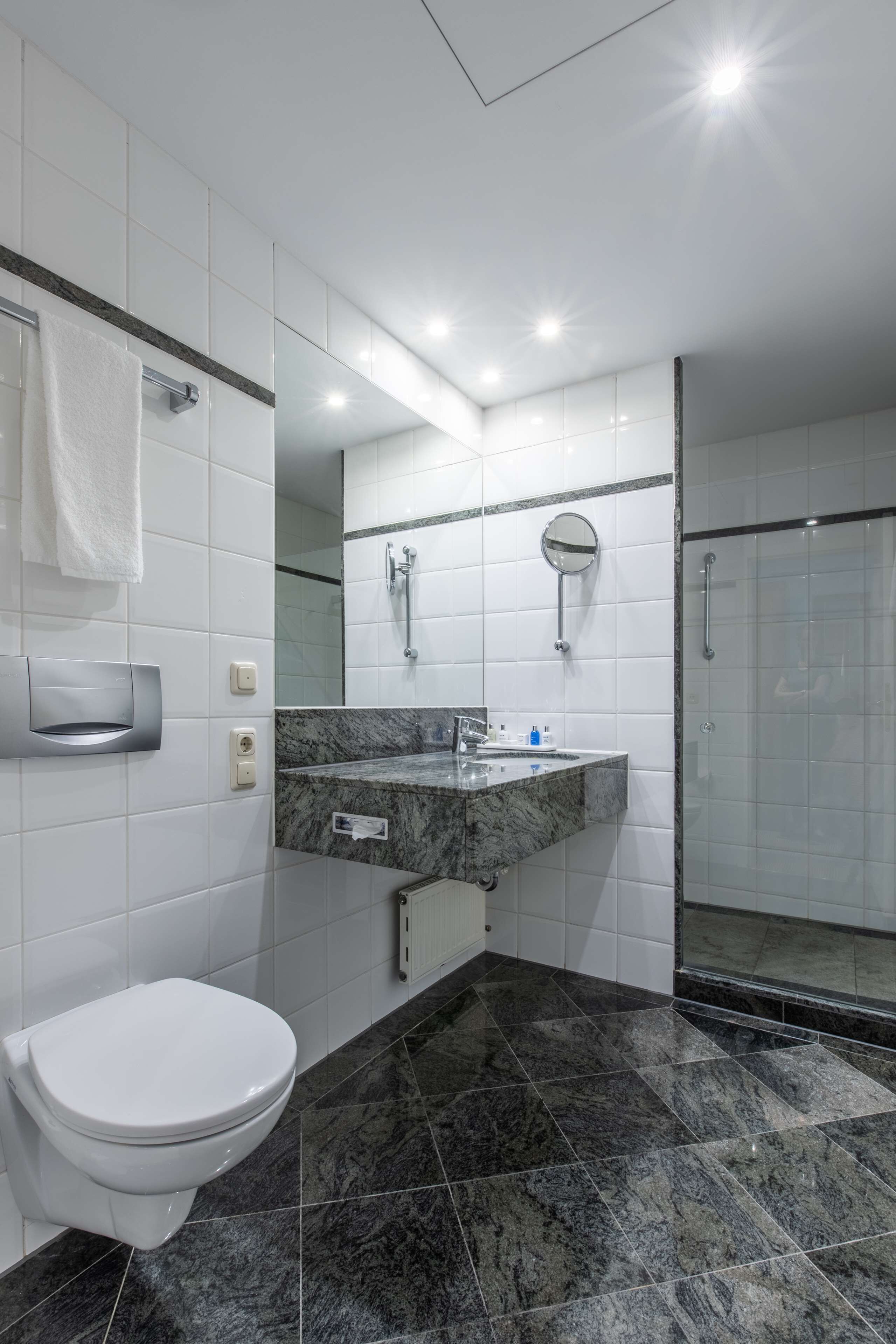 Un baño moderno con inodoro blanco, lavamanos de mármol, cabina de ducha de vidrio y espejo sobre el lavamanos.