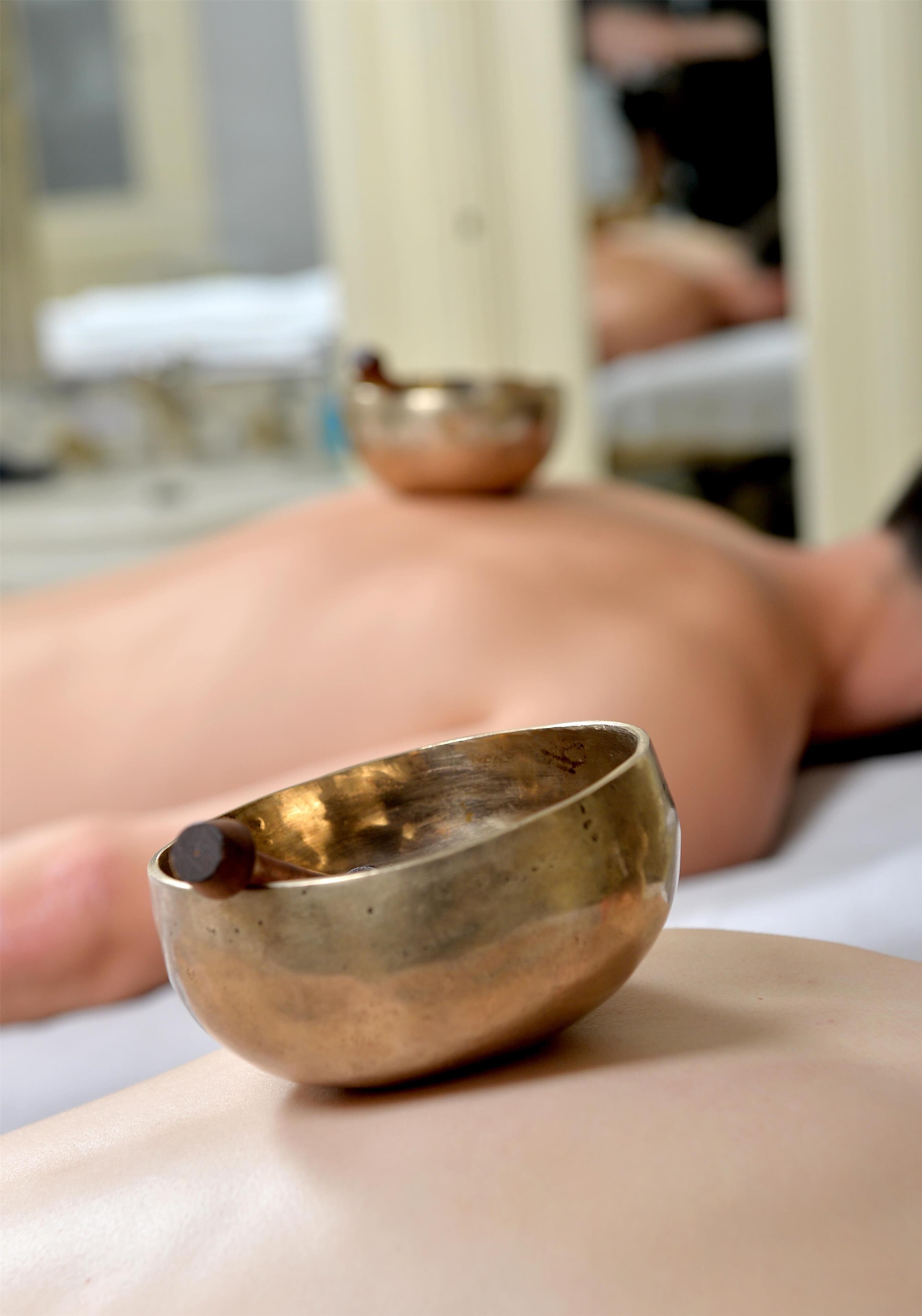 A massage therapy session with a person lying face down, a small metallic bowl, and a massage table.